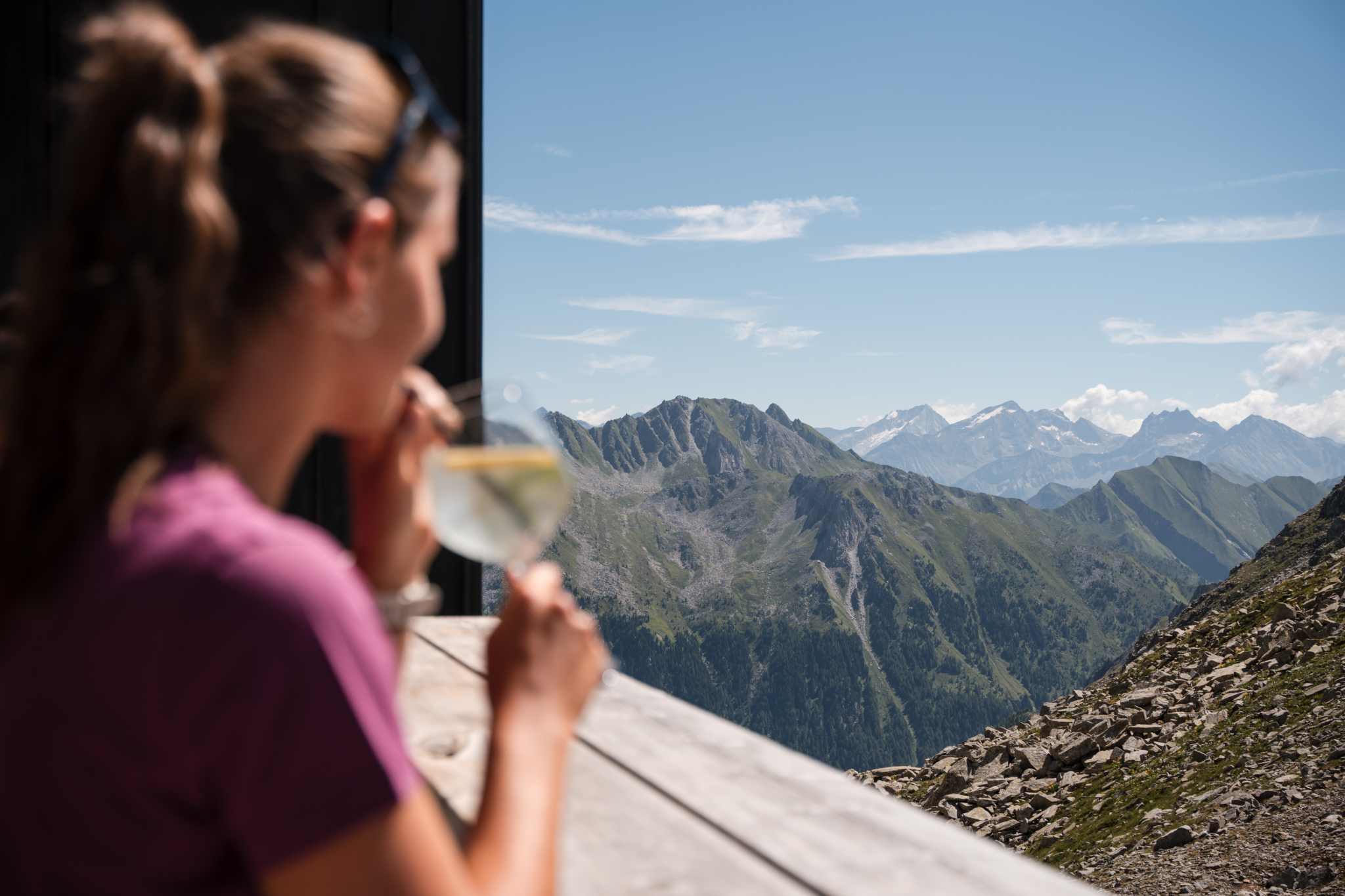Frau genießt ein Getränk auf einer sonnigen Terrasse mit Blick auf die Berge